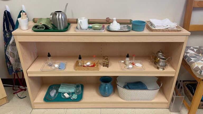 A carefully arranged Montessori classroom shelf with child-sized trays and practical life materials on light wood shelving.
